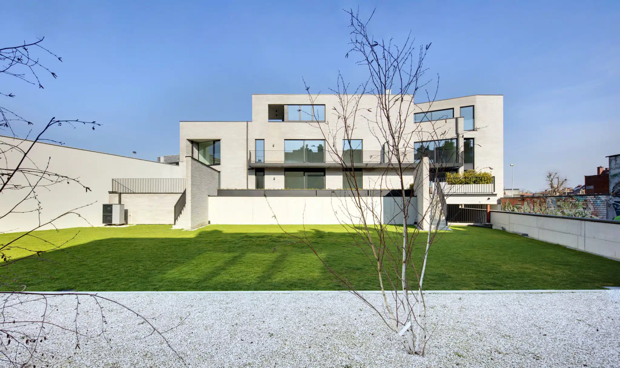 Moderne appartementsgebouw met witte gevelbekleding, grote raampartijen en groene tuin in Sint-Niklaas, ontworpen door ONA Ar