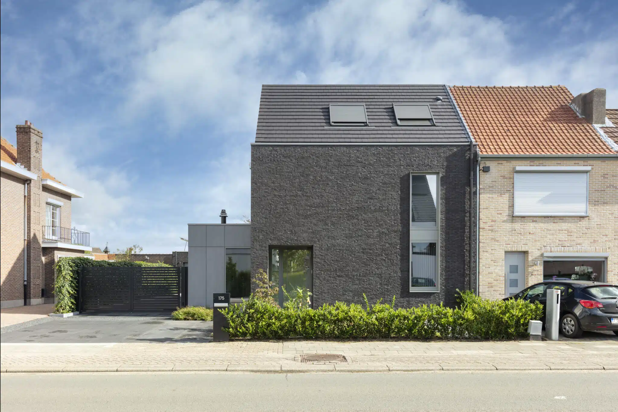 Moderne woning Sint-Niklaas met donkere natuurstenen gevel, dakvensters en strakke architectuur door ONA Architecten Beveren