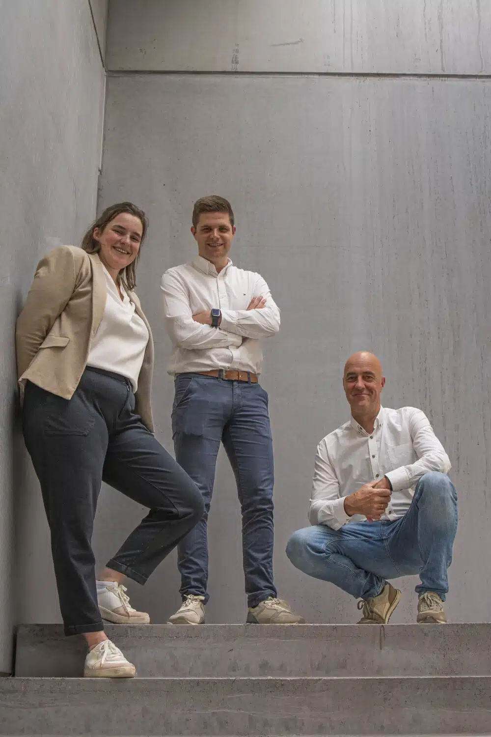 Het team van ONA architecten: Flore Cotton, Michiel Mertens en Serge Chiapparo poseren op betonnen trappen in Beveren.