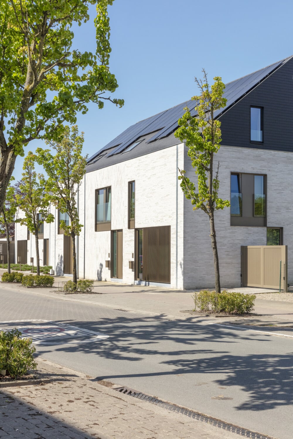 Straatbeeld van 7 BEN-nieuwbouwwoningen in Temse-Velle met lichte gevelsteen, donker dak met zonnepanelen en groene voortuine