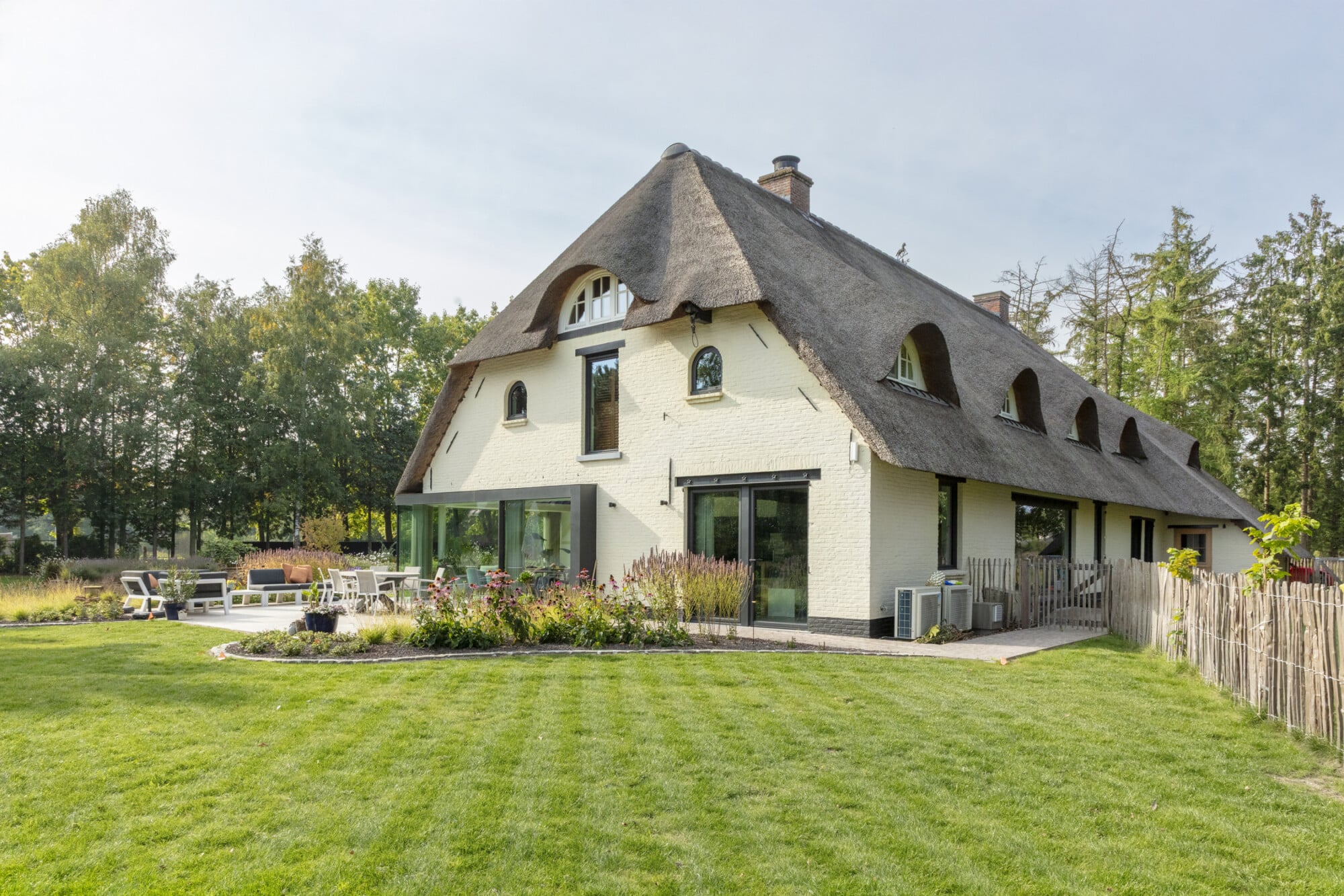 Gerenoveerde landelijke hoeve in Stekene met rieten dak, witte gevelsteen, grote raampartijen en verzorgde tuin — ONA Archite