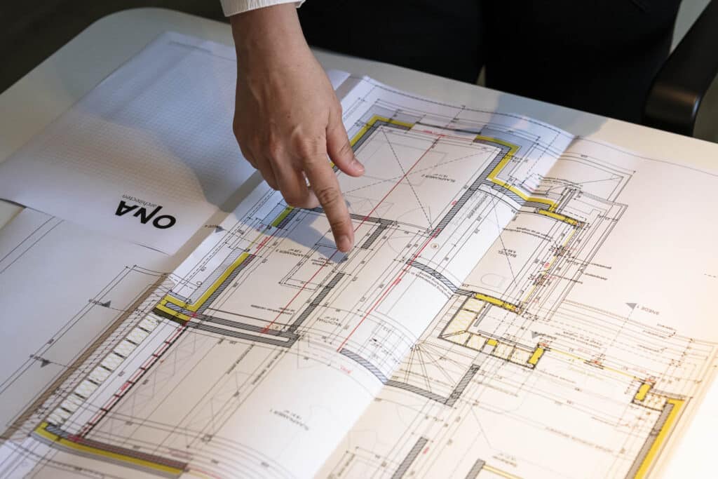 Architect van ONA Architecten wijst details aan op een bouwplan met plattegrond, uitgewerkt tot in de puntjes voor een archit