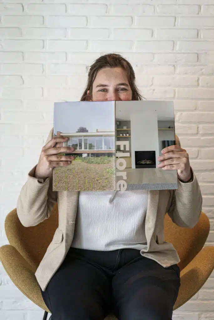 Flore, architect bij ONA Architecten in Beveren, houdt een architectuurboek vast voor haar gezicht in het kantoor