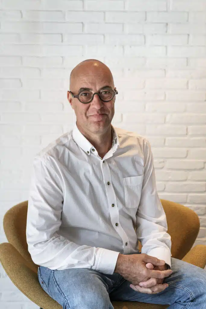Serge Chiapparo, architect en oprichter van ONA Architecten in Beveren, zittend in een gele fauteuil voor een witte