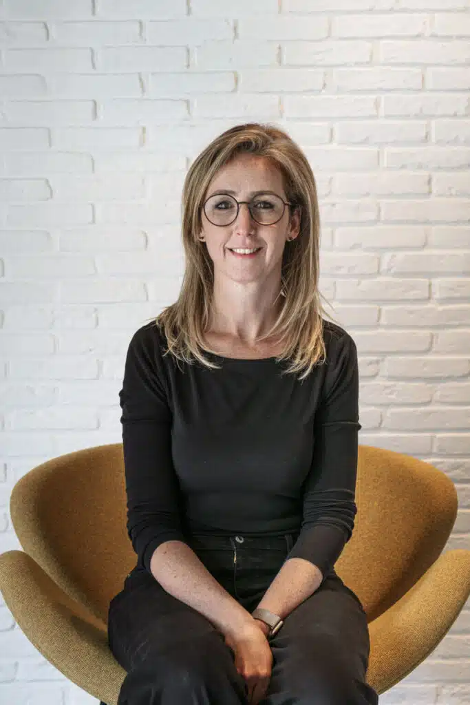 Flore Cotton, architect-vennoot bij ONA Architecten Beveren, zittend in gele stoel tegen witte bakstenen muur