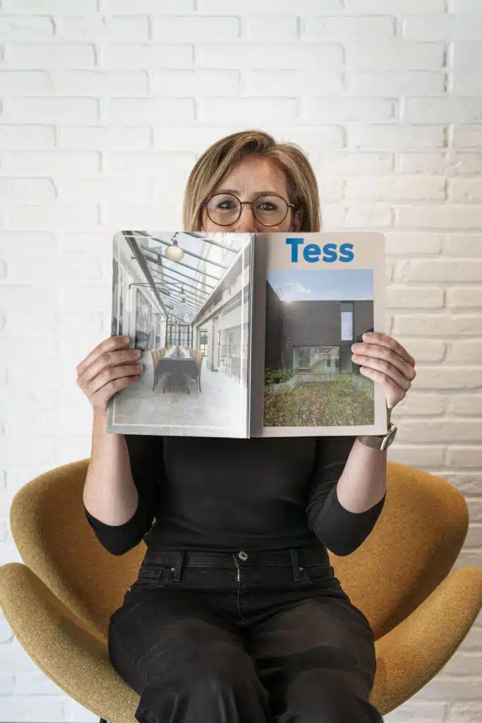 Tess, architect bij ONA Architecten in Beveren, zittend met een architectuurmagazine voor haar gezicht in het kantoor.