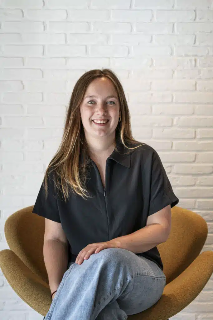 Tess, architect bij ONA Architecten in Beveren, zittend in een gouden fauteuil voor een witte bakstenen muur
